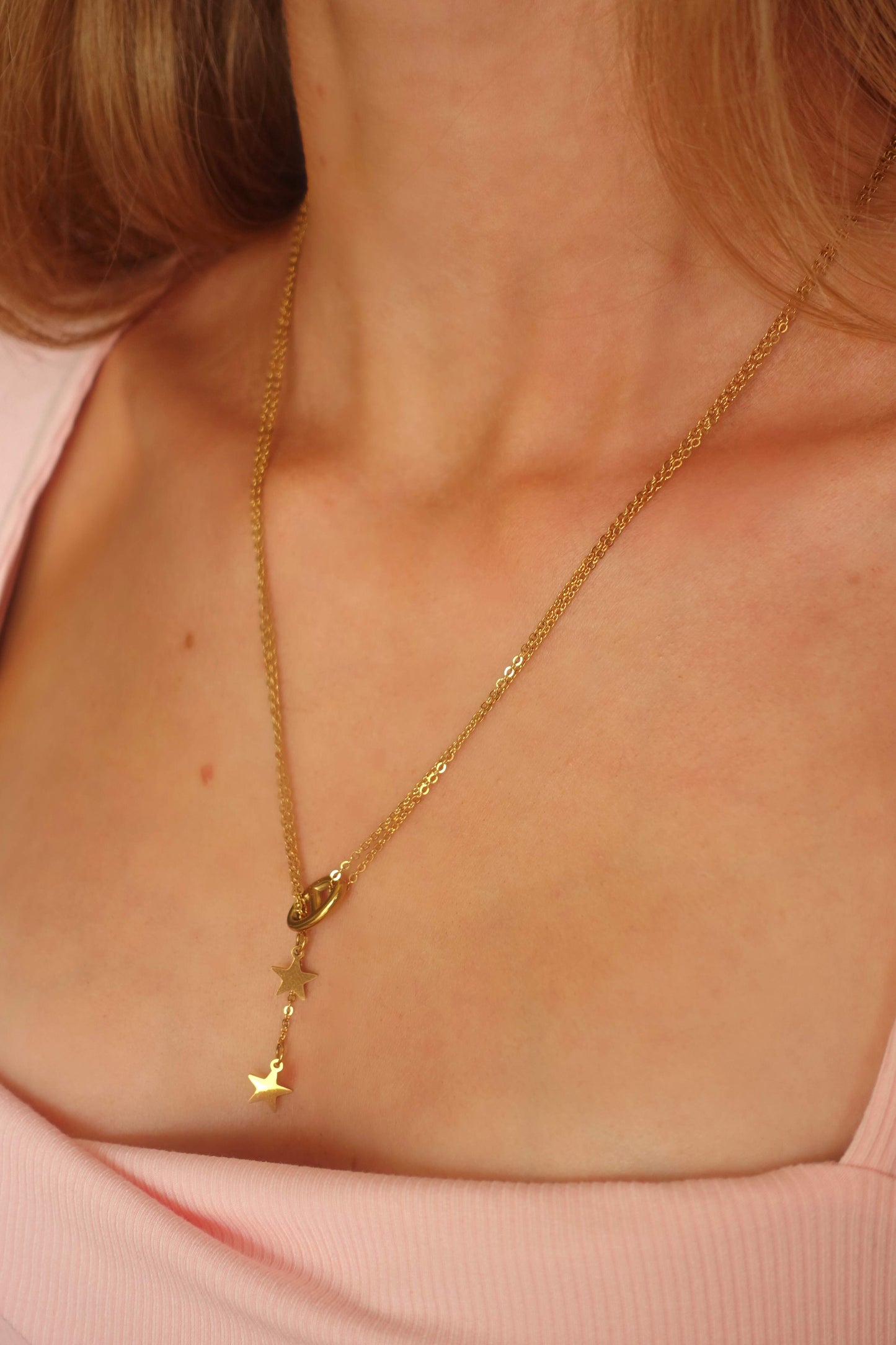 Collier "Star Muse" porté. Design en Y avec pendentifs étoiles, ajusté au cou. Look féminin et raffiné, bijou doré en acier inoxydable.