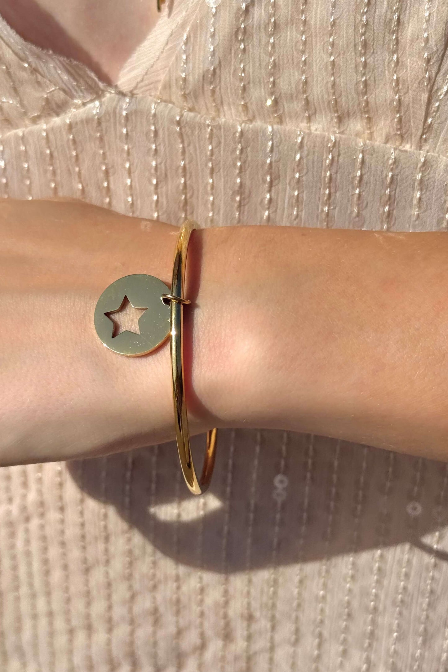 Bracelet jonc en acier inoxydable doré avec une breloque élégante. Taille unique, diamètre de 70 mm. Disponible chez Sisters Bay