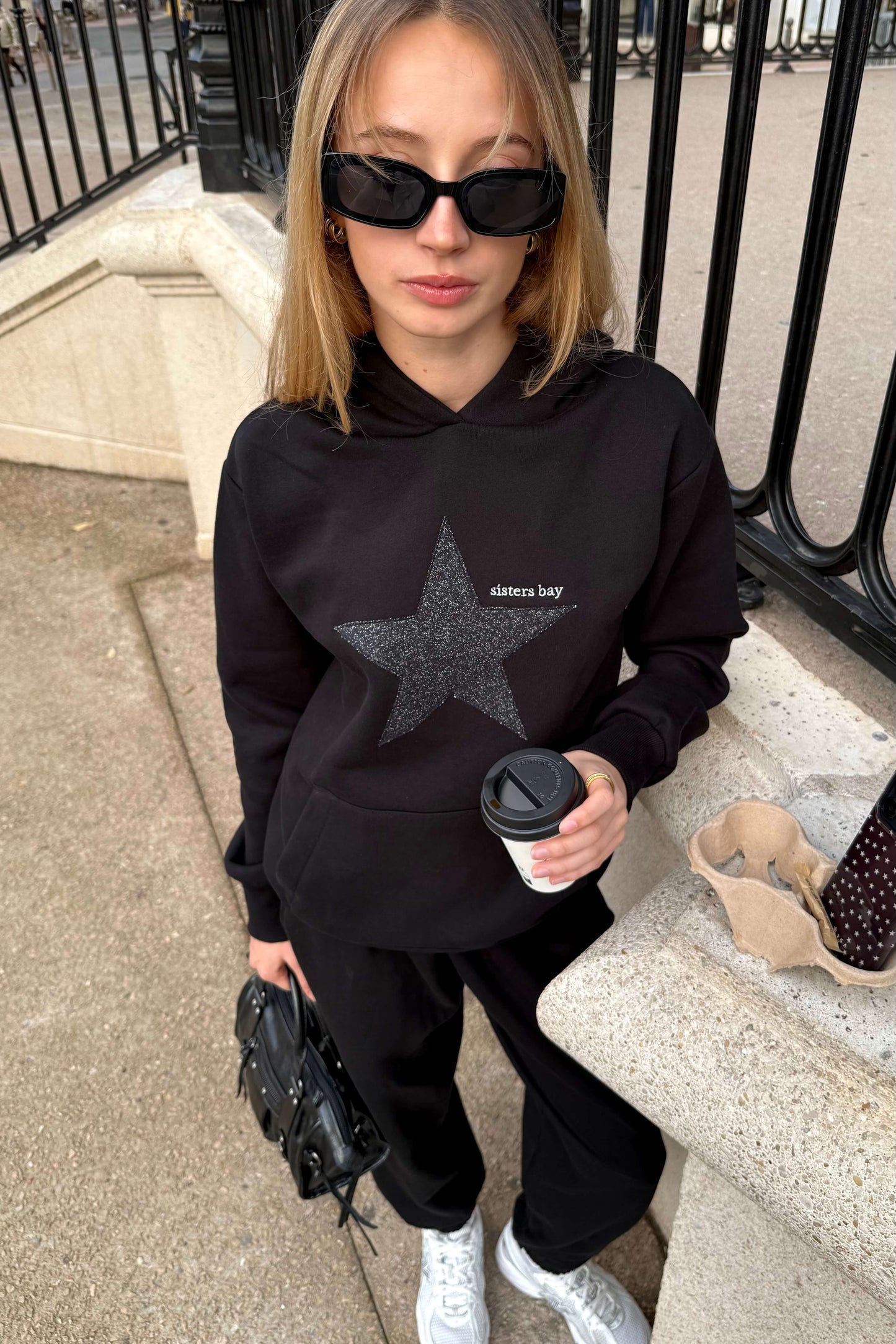 Hoodie noir femme Sisters Bay, broderie argentée premium et capuche. Sweat écoresponsable avec poche kangourou + rangement téléphone. Mode, confort, qualité.