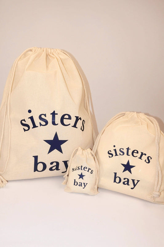 Trois pochons cadeau Sisters Bay en tissu réutilisable. Logo navy et cordons resserrables. Disponibles en tailles 1, 2 et 3.