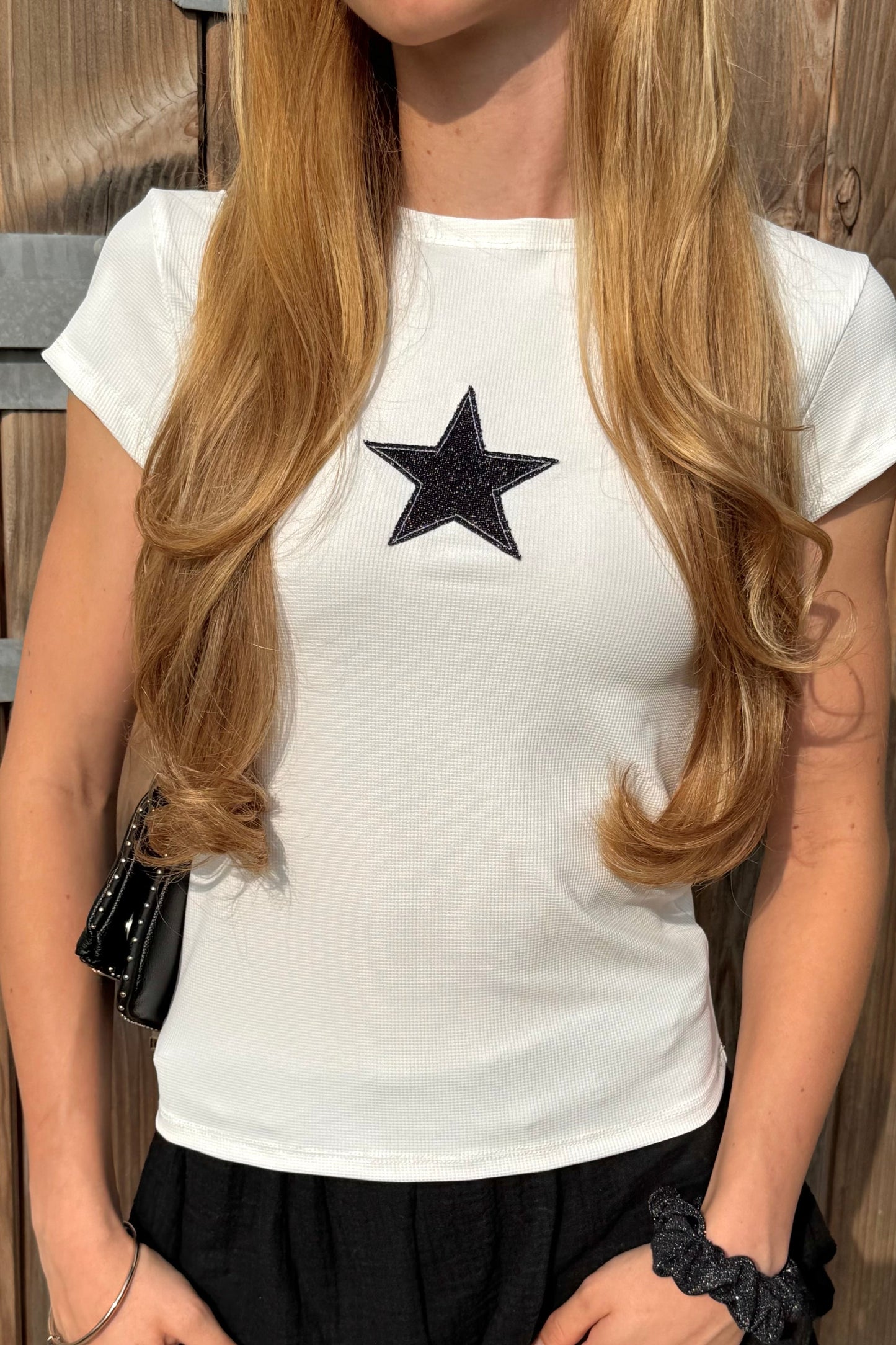 Femme portant le T-shirt blanc cassé Stargirl de Sisters Bay, coupe cintrée, col rond, étoile noire pailletée sur la poitrine, en coton gaufré.