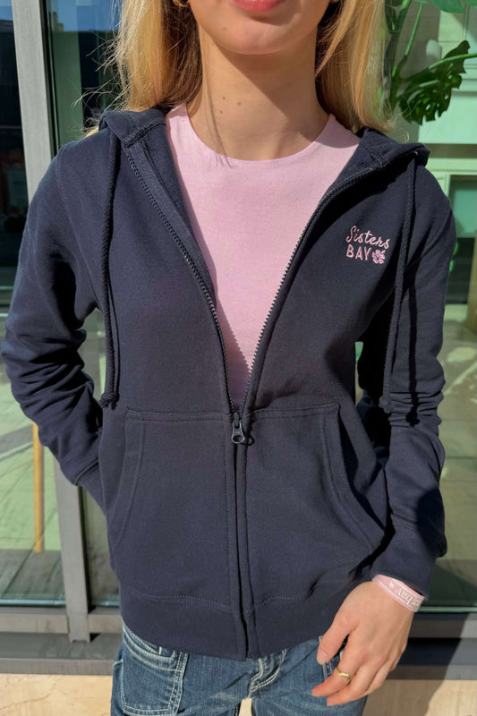 Veste Paradise zippée création exclusive Sisters Bay, coupe ajustée avec capuche, brodée à l’avant dans notre atelier avec logo rose Sisters Bay et fleur d’hibiscus. Modèle confortable en coton ringspun et polyester, existe aussi en gris.